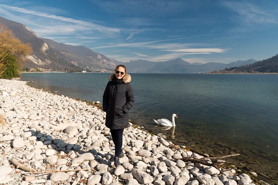 lady by lake Iseo in Italy with mountains and a swan in the background during a babymoon