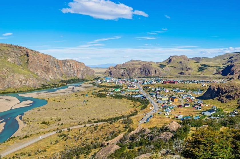 view of el chalten during day with a river on the left and mountains all around